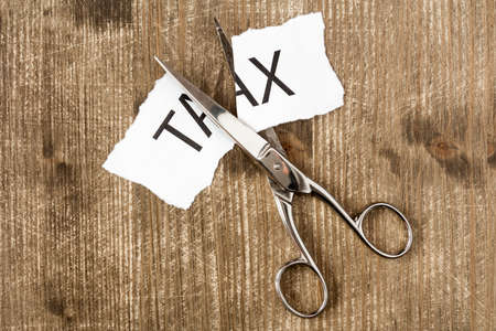 Scissors are cutting a piece of paper with the word taxの写真素材