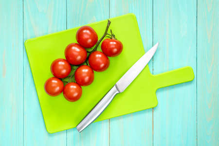 The branch of cherry tomatoes and knife on a cutting boardの写真素材