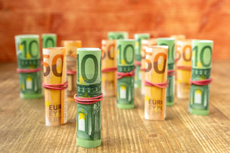 Several euro banknotes rolled up and stacked on wooden backgroundの写真素材