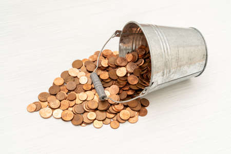 Euro cents spilling from metal bucket on wooden table