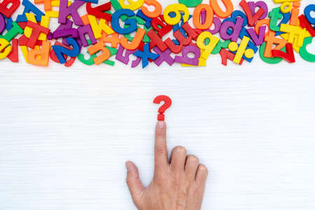 Hand with question mark on the table with many plastic numbers and letters. Concept for confusion or curiosity.の写真素材