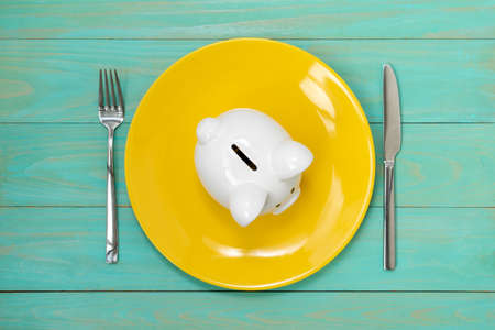 Savings consumer concept. Piggy bank on the yellow plate with fork and knife.の写真素材
