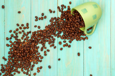 Green cup with scattered coffee beansの写真素材