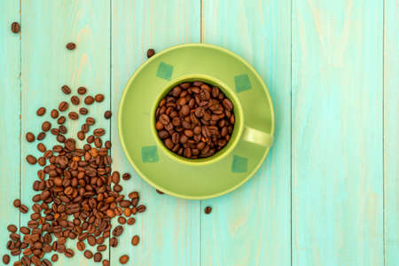 Green cup and coffee beans on wooden background. Top view.の写真素材
