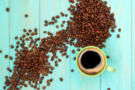 Green cup of coffee and coffee beans on wooden background. Top view.の写真素材