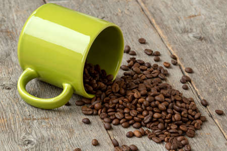 Green mug with scattered coffee beans on wooden backgroundの写真素材