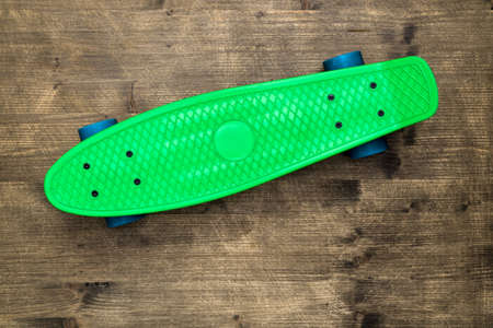 Green skateboard on wooden background, top view