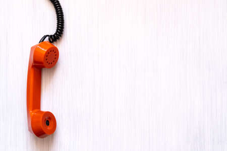 Orange phone handle hanging down on a cord. Urgent business. Unsolved problem. Getting in touch.の写真素材