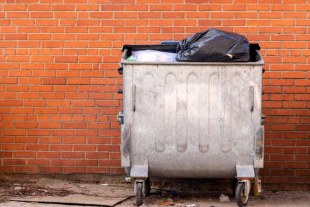 Trashcan full of garbage, standing over brick wall