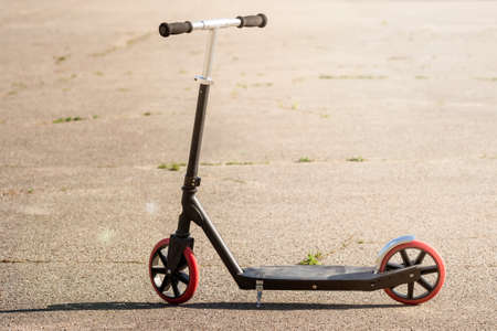 Kick scooter on the asphalt. Black kick scooter with red wheels. Sport activity on summer time.の写真素材