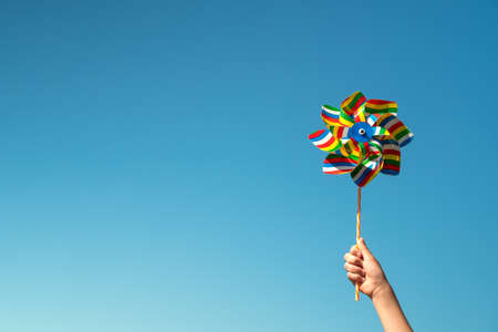 Child holds colorful pinwheel on blue sky backgroundの写真素材