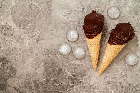 Chocolate ice cream in wafer cone and ice pieces on grey backgroundの写真素材