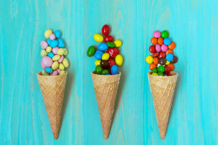 Three wafer cones with colored candy on wooden background
