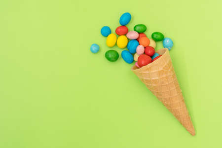 Waffle horn with colored candy on green background. Top view, copy-space