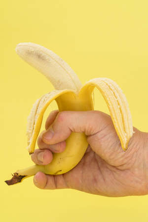 Human hand holding banana on yellow background. Nutrition or healthy food conceptの写真素材