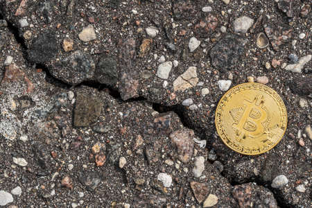 Shiny golden bitcoin on cracked pavement. Crack goes down as cryptocurrency crash concept