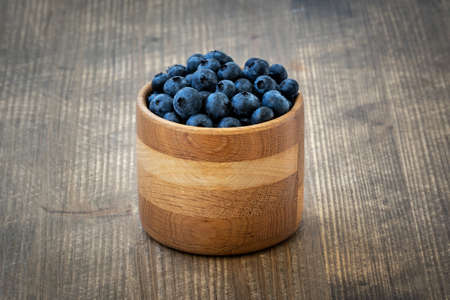Freshly picked blueberries in wooden bowl on wooden background. Healthy eating and nutrition.の写真素材