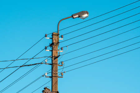 High voltage electric pole with lamp over a sky background