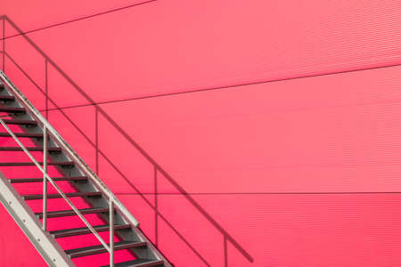 Iron staircase for up to maintenance work or fire escape. Steel stairs are on the side of the pink wall.の写真素材