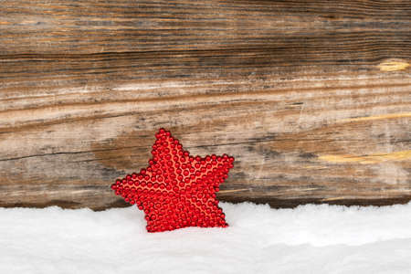 Red Christmas decorations star in the snow against wooden backgroundの写真素材