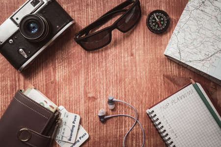 Go on an adventure! The map, old camera, wallet, compass, sunglasses and notebook on a wooden table....
