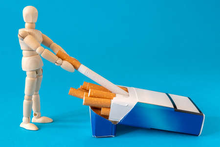 Wooden man takes a cigarette from a cigarettes pack.Cigarette addiction. Tobacco nicotine smoke....