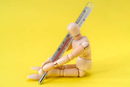 Wooden man holding a thermometer on a yellow background.