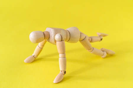 Wooden man doing push-ups on the yellow background. Healthy life concept.