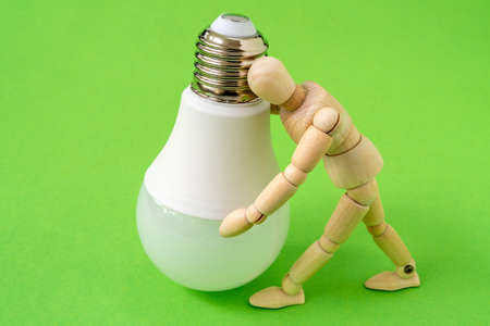 Wooden man holds a LED light bulb. Using economical and environmentally friendly light bulb concept.の写真素材