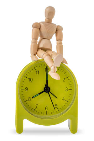 Wooden mannequin sits on green alarm clock isolated on white backgroundの写真素材