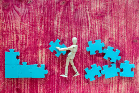 Wooden man with puzzle on pink background. Building a business success.の写真素材
