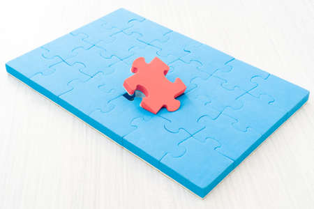 Red color puzzle piece standing out from larger group of blue puzzle pieces. Business concept and...