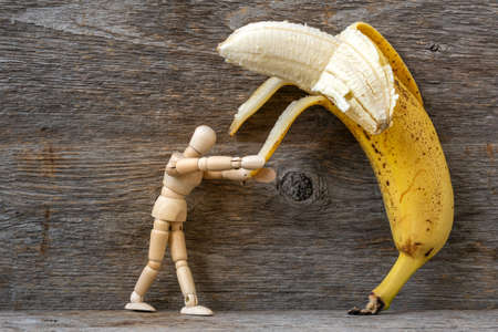 Wooden mannequin peeling a banana. Healthy eating concept.の写真素材