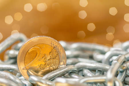 Two Euros Coin with a metal chain on a gold backgroundの写真素材