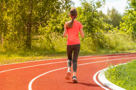Fitness girl running in the stadium. She is running on a warm summer afternoon. Young athlete doing her routine sports practice on a track.の写真素材
