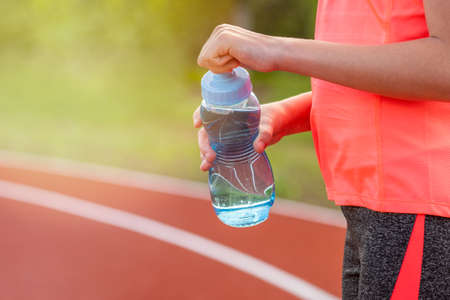 Thirst and water balance concept. Girl holding bottle of water on running track on the stadium.