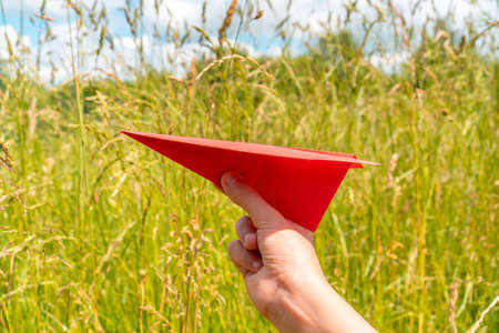Plane paper in children hand, middle in grassland. Travel conceptの写真素材