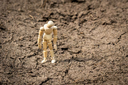Wooden man standing on soil dry land, looking sad and frustrated thinking about problemsの写真素材