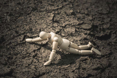 Wooden man lying on cracked earth in the arid area. Thirst and dehydration.の写真素材