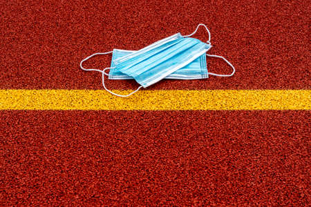 Medical masks lying behind the yellow line in the sports ground. Stay safe concept. Cancellation of...