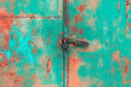 Old rusted grungy metal garage door with latch and padlock. Close up of rusty vintage lock on closed...