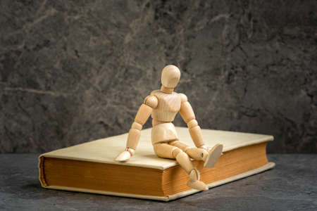 Wooden man sitting on the book. Literature research. Concept - information search in books.の写真素材