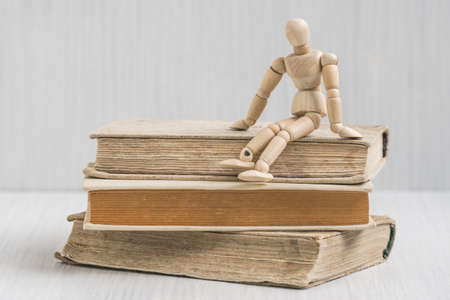 Wooden man sitting on the books stack. Literature research. Concept - information search in books.