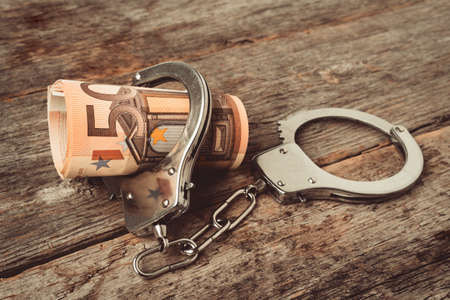Roll euro money bills on a wooden table in handcuffs. Handcuffs and money on table. Financial crime,...