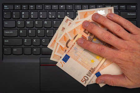 Conceptual shot of businessman's hand taking euro banknotes from computer keyboard. Financial help or government aid, for people affected by the crisisの写真素材