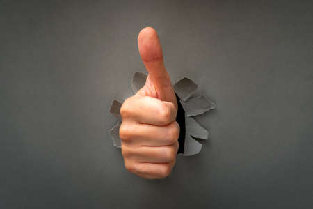 Thumbs up through the hole in a grey paper sheet