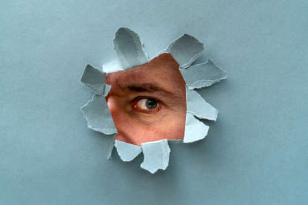 The human eye is watching us through a hole in a grey paperの写真素材