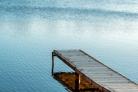 Wooden pier on the lake. Wooden bridge in autumn time with calm lake. Lake for fishing and recreation with pier.の写真素材