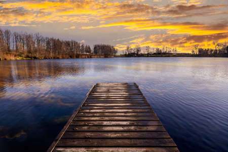 Sunset over the lake in the nature. View from a wooden bridge. Beautiful sky reflection on the...