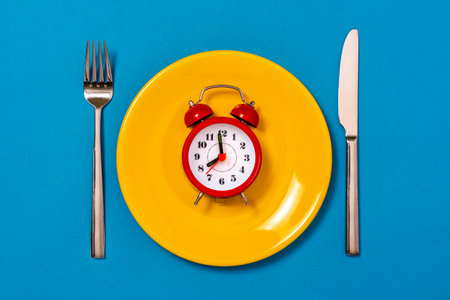 Alarm clock on yellow plate with fork and knife. Intermittent fasting, Ketogenic dieting, weight loss, meal plan and healthy food conceptの写真素材